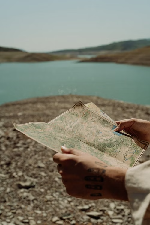 Hands holding a paper map beside a lake